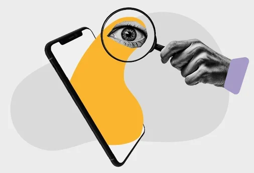 Uma mão segura uma lupa sobre um dispositivo móvel.