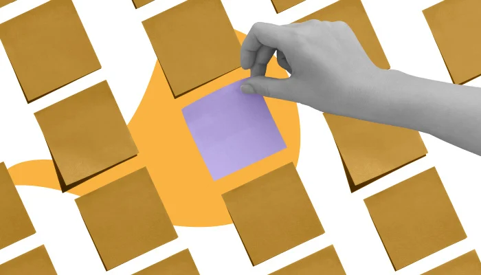 Uma mão coloca um post-it roxo em meio a uma série de post its amarelos.